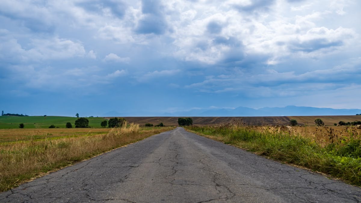 A tranquil rural road in Žilina, Slovakia stretches through lush countryside under a dramatic sky.